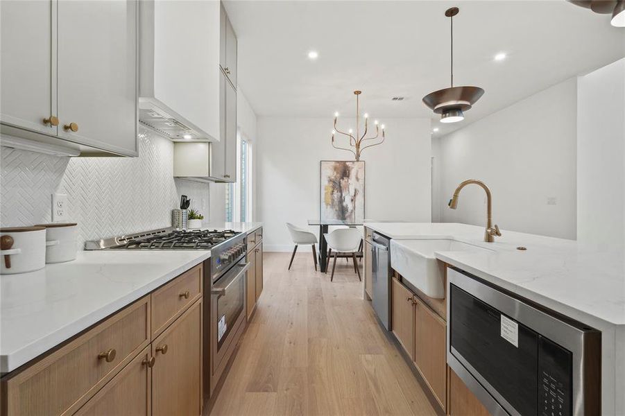 Kitchen featuring stainless steel appliances, light stone counters, hanging light fixtures, light wood-style flooring, and recessed lighting