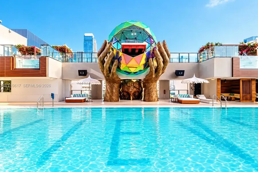 Rooftop swimming pool featuring a geometric glass dome sculpture, integrated bronze-finished hand statues, wood-panel siding, and glass railings Rooftop swimming pool featuring a geometric glass dome sculpture, integrated bronze-finished hand statues, wood-panel siding, and glass railings