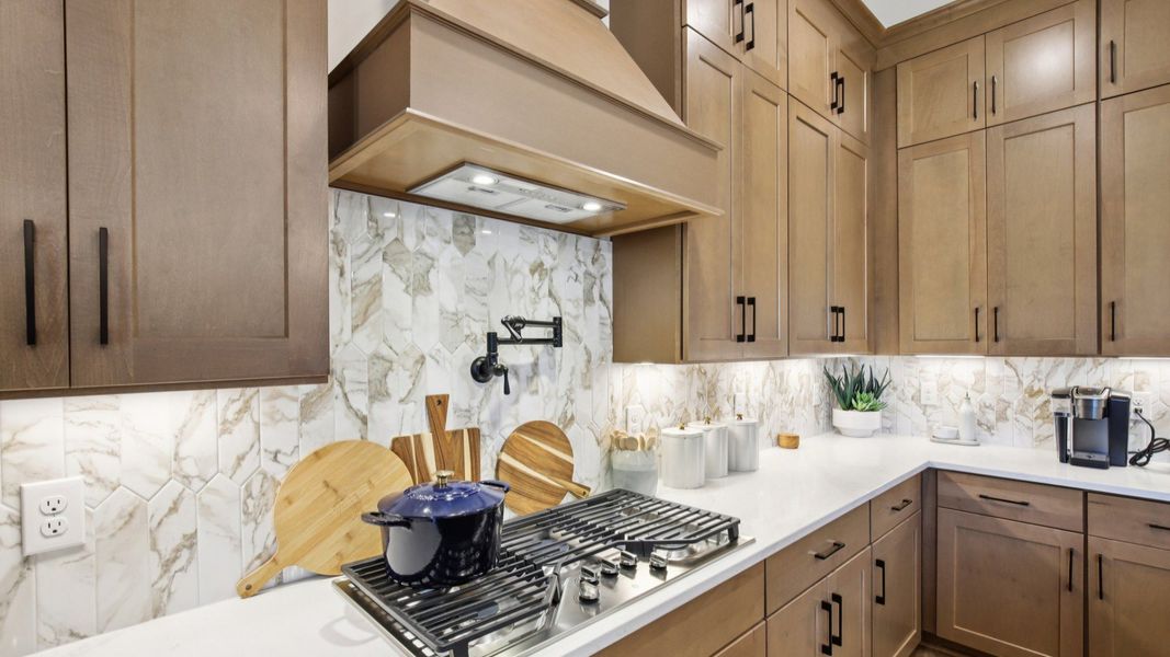 Kitchen with white quartz countertops, tile backsplash, and natural wood cabinets