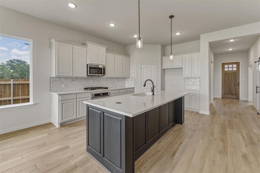 Kitchen featuring a central island with white countertop, white cabinetry, integrated stainless steel microwave, gas range, and wood-finish flooring Kitchen featuring a central island with white countertop, white cabinetry, integrated stainless steel microwave, gas range, and wood-finish flooring