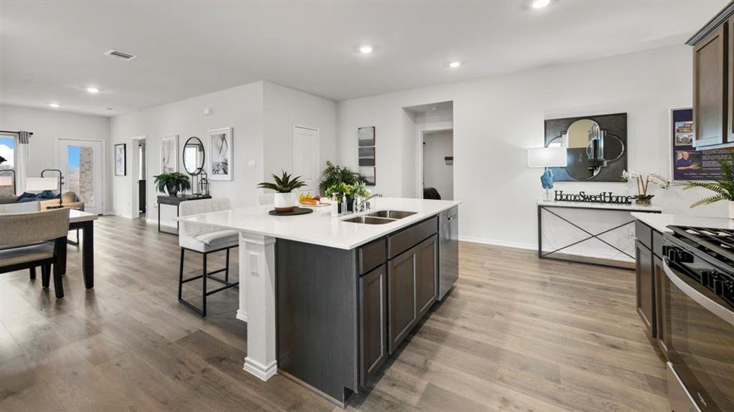 Spacious kitchen featuring a central island with a solid surface countertop, dark wood-finish cabinetry, stainless steel appliances, and wood-finish flooring Spacious kitchen featuring a central island with a solid surface countertop, dark wood-finish cabinetry, stainless steel appliances, and wood-finish flooring