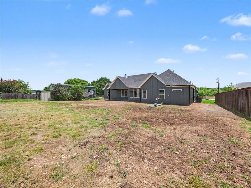 Expansive rear property with a dark-tone siding residence featuring multiple windows and a dark shingle roof Expansive rear property with a dark-tone siding residence featuring multiple windows and a dark shingle roof