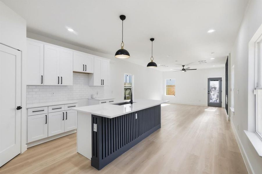 Kitchen with white cabinets, light wood finished floors, a kitchen island with sink, light stone countertops, and hanging light fixtures