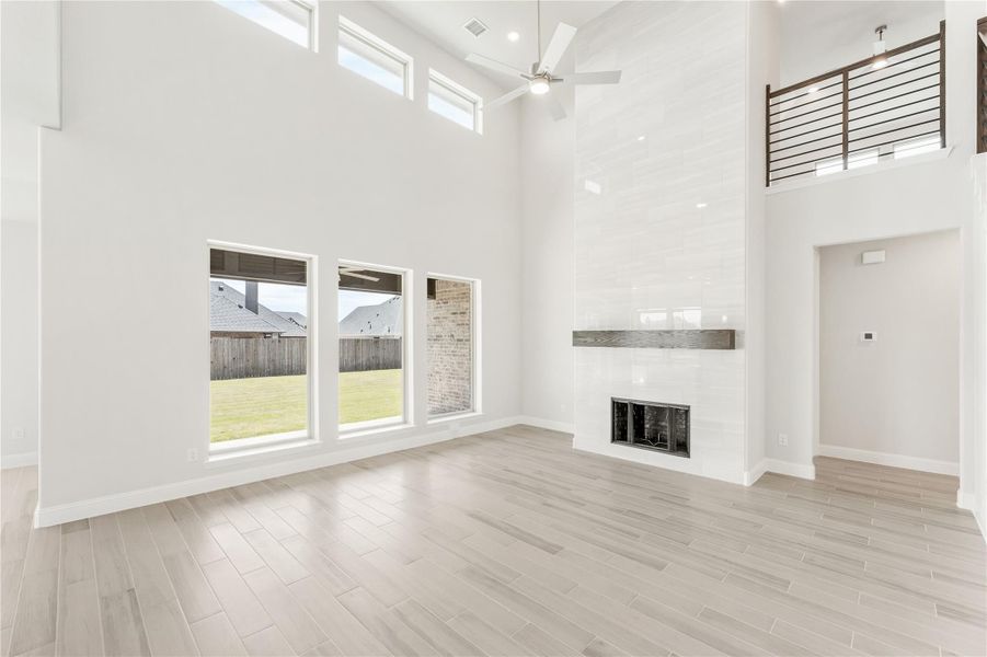 Open living room with two-story ceiling, fireplace, light wood floors, and large windows overlooking backyard Open living room with two-story ceiling, fireplace, light wood floors, and large windows overlooking backyard