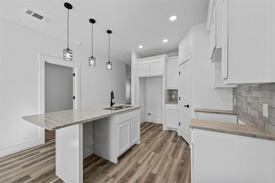 Kitchen featuring decorative backsplash, white cabinetry, sink, and an island with sink