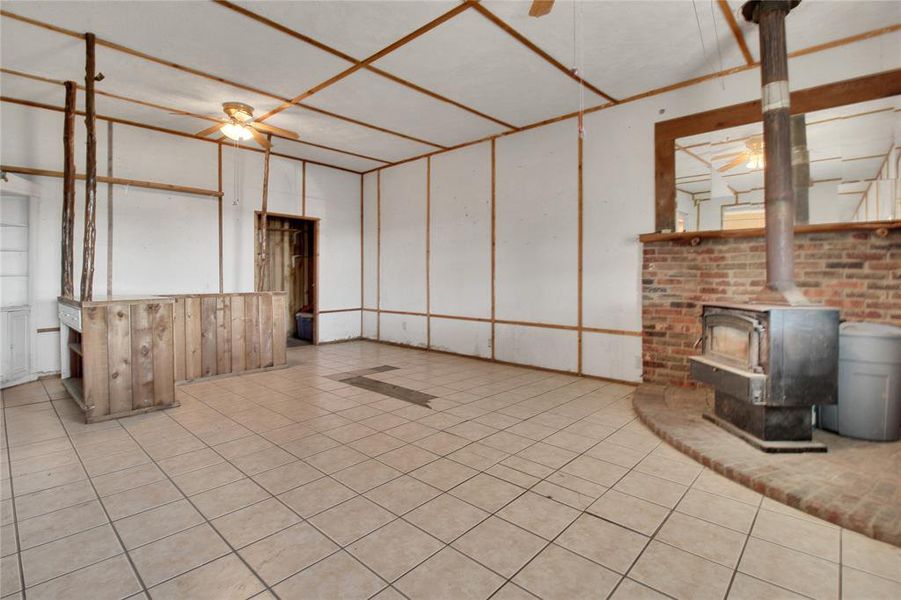 Unfurnished living room featuring ceiling fan, a wood stove, and tile patterned flooring Unfurnished living room featuring ceiling fan, a wood stove, and tile patterned flooring