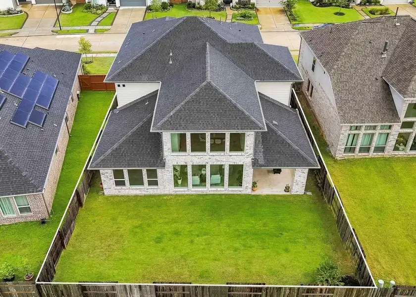 This aerial view highlights the expansive, fully fenced backyard, offering generous space for recreation, entertaining or future enhancements, while a covered patio provides a shaded setting for outdoor dining and relaxation.