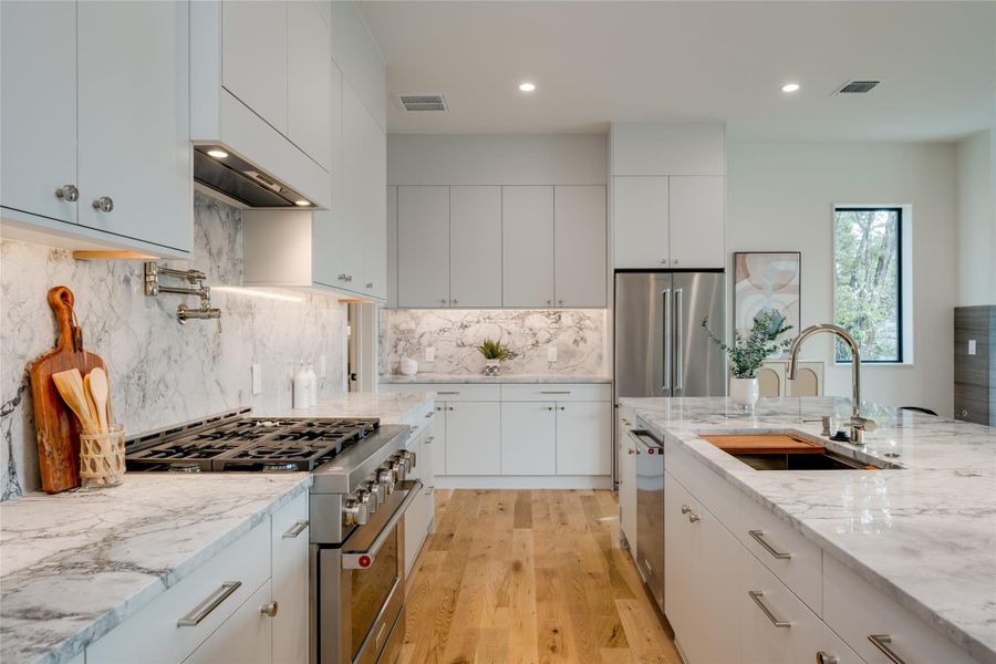 Kitchen with high end appliances, light stone countertops, white cabinets, and sink