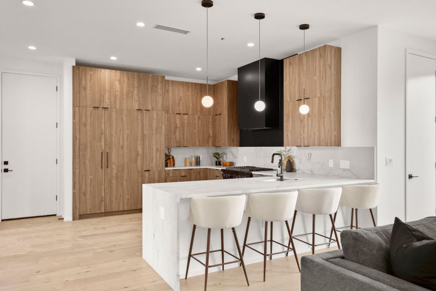 Kitchen with a breakfast bar, modern cabinets, a peninsula, light stone counters, and light wood finished floors