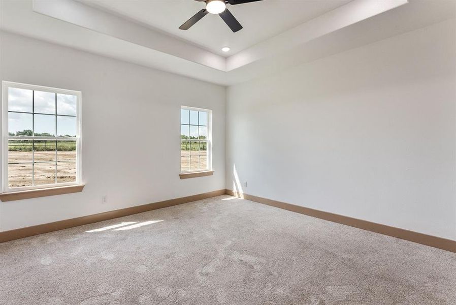 Carpeted empty room with a raised ceiling and ceiling fan Carpeted empty room with a raised ceiling and ceiling fan