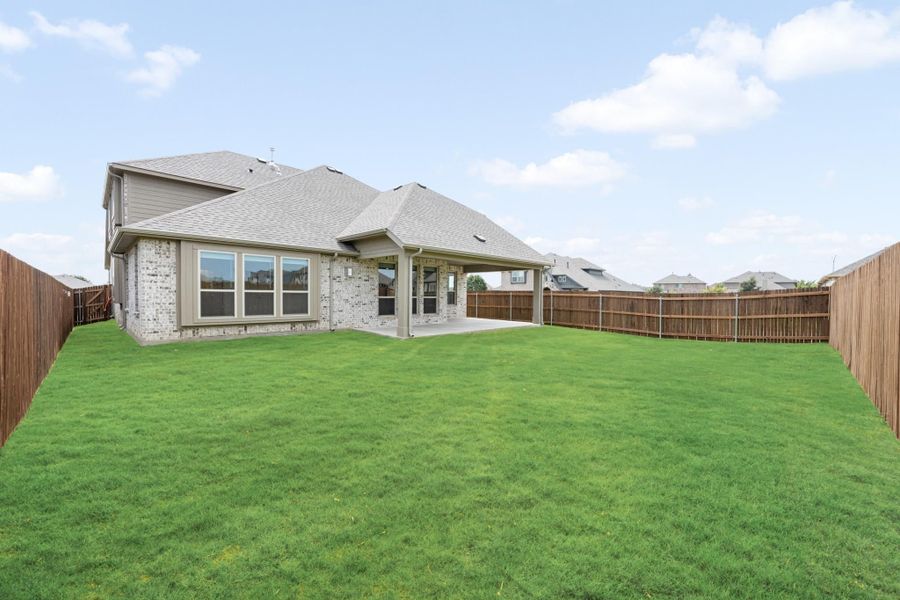 Backyard of brick home with large green lawn, covered patio, and wood privacy fence