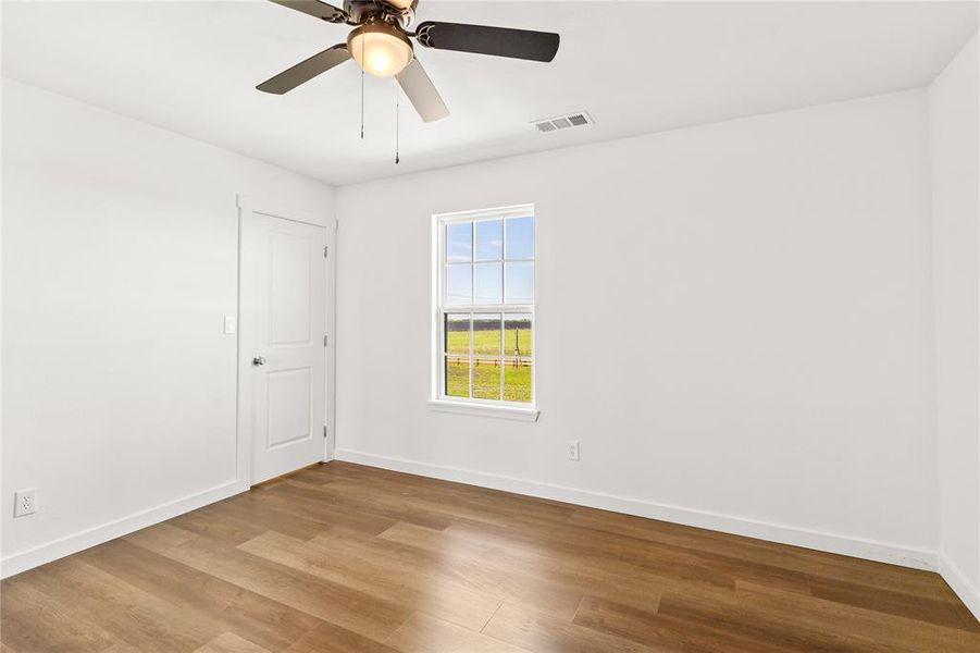 Bright interior space featuring wood-finish flooring, a ceiling fan with integrated lighting, and a window with outdoor scenery
