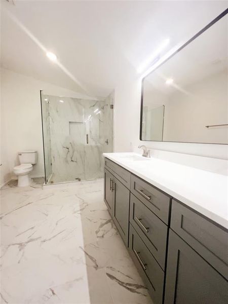 Modern bathroom featuring a double vanity with grey cabinetry and white countertop, large walk-in shower with glass enclosure and marble-look tile, and recessed lighting