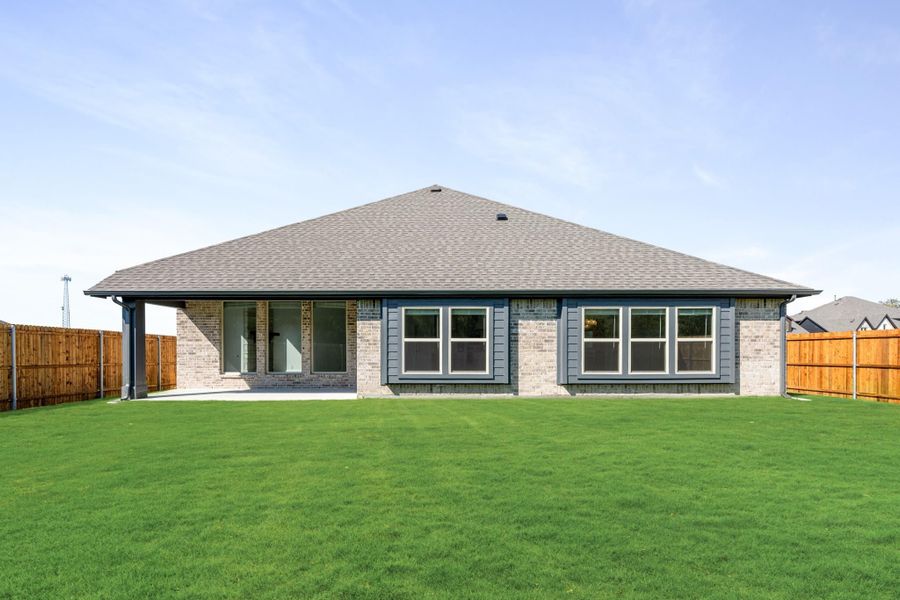 Rear view of single-story brick home with hip roof, large windows, covered patio, and fenced backyard with green lawn Rear view of single-story brick home with hip roof, large windows, covered patio, and fenced backyard with green lawn