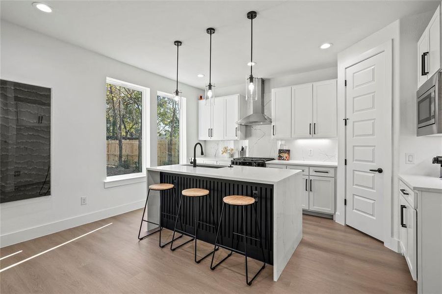 Kitchen featuring white cabinets, wall chimney exhaust hood, and a center island with sink