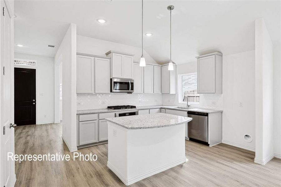 Modern kitchen featuring light wood-finish flooring, white cabinetry with crown molding, stainless steel appliances, and a central island with a granite-style countertop