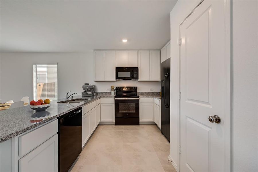 Kitchen with white cabinetry, sink, black appliances, kitchen peninsula, and light stone counters