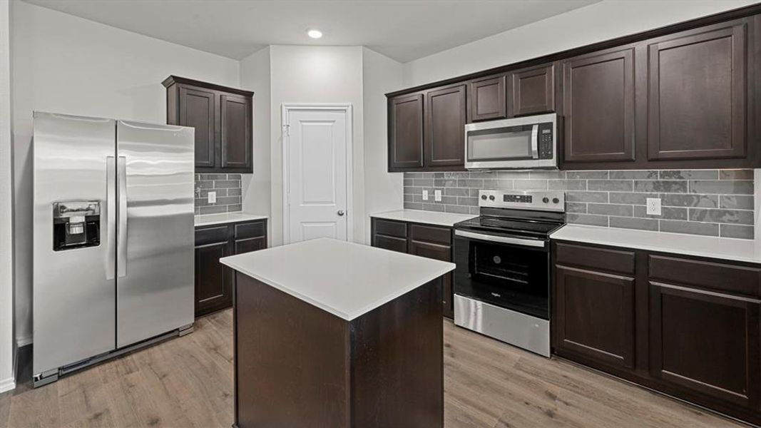 Kitchen featuring stainless steel appliances, dark wood finish cabinetry, a kitchen island, decorative backsplash, and recessed lighting