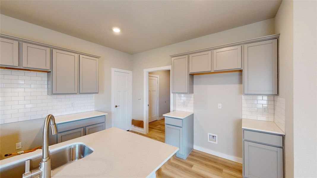 Kitchen with decorative backsplash, gray cabinets, light wood-style flooring, light stone counters, and recessed lighting