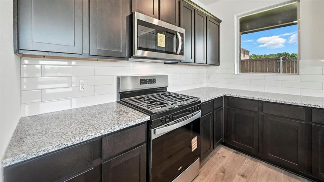 Kitchen with stainless steel appliances, tasteful backsplash, light stone counters, and light wood-style flooring