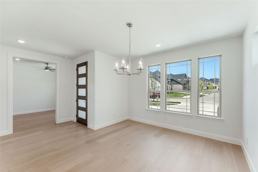 Empty dining room with chandelier, hardwood floors, large windows, and a dark wood door with glass panels