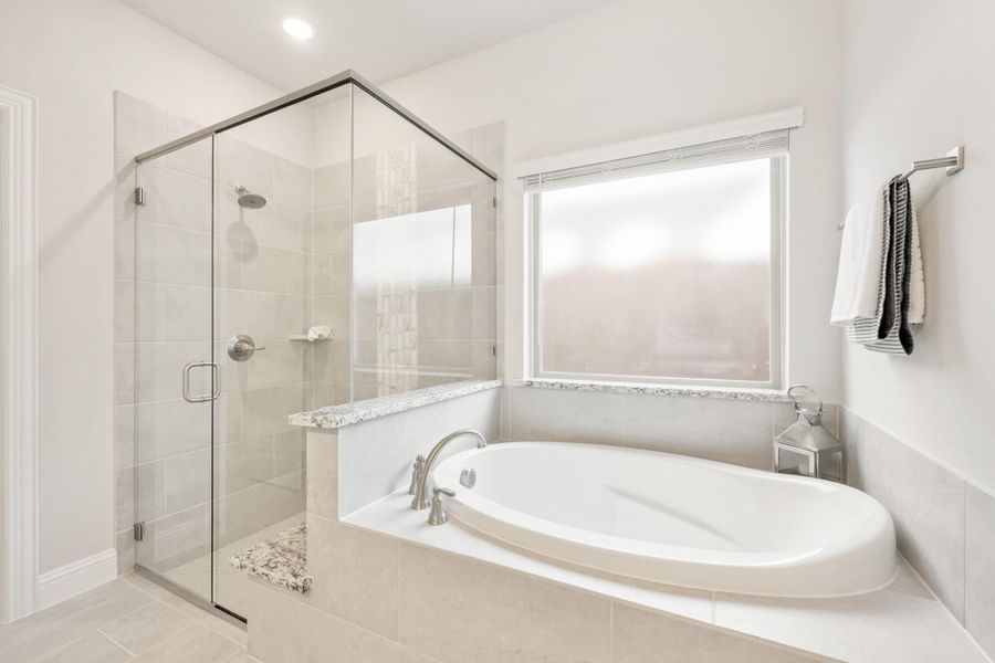 Master bathroom with soaking tub, glass-enclosed shower, and tile floors in white and beige tones
