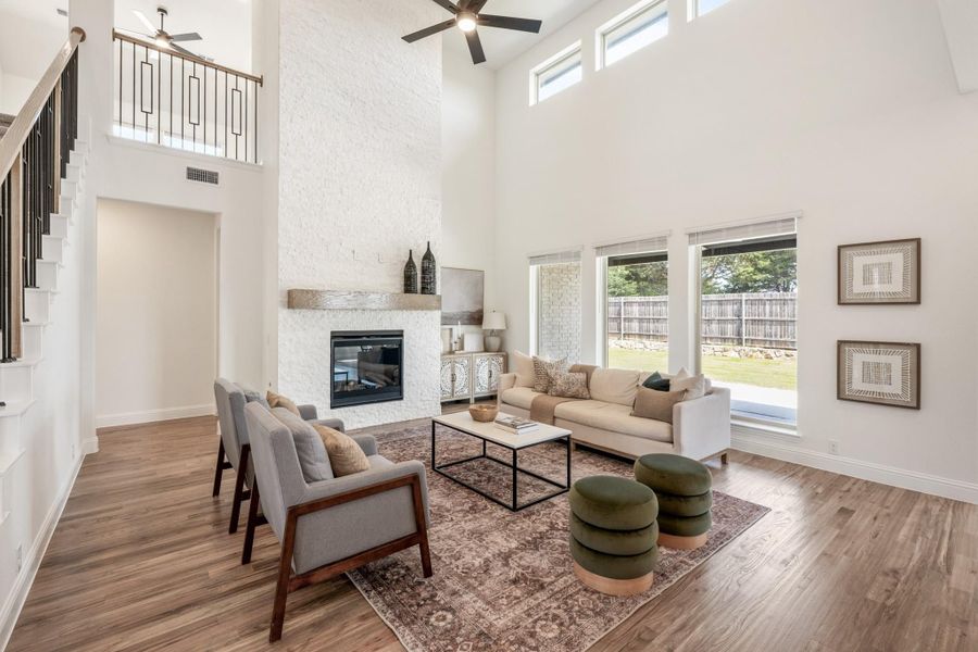 Living room with two-story ceiling, white stone fireplace, hardwood floors, and large windows overlooking backyard