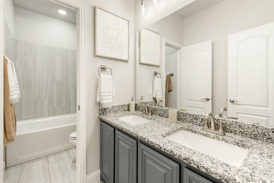 Bathroom with double sink vanity, granite countertops, gray cabinets, and tiled shower-tub combo
