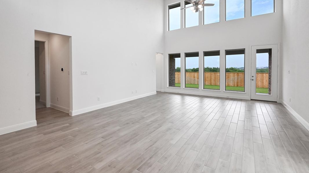 Unfurnished living room featuring a high ceiling, ceiling fan, baseboards, and light wood-type flooring