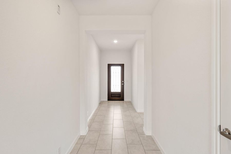Narrow hallway with white walls, tile floors, and dark wood front door with glass panel