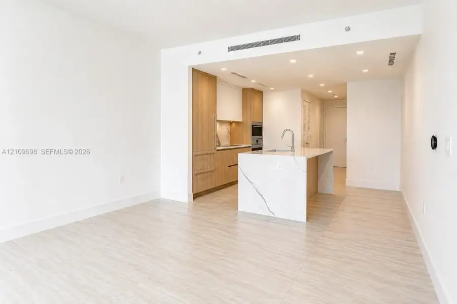 Kitchen featuring wood-finish cabinetry, stone-surface waterfall island with an undermount sink, built-in appliances, recessed lighting, and tile flooring