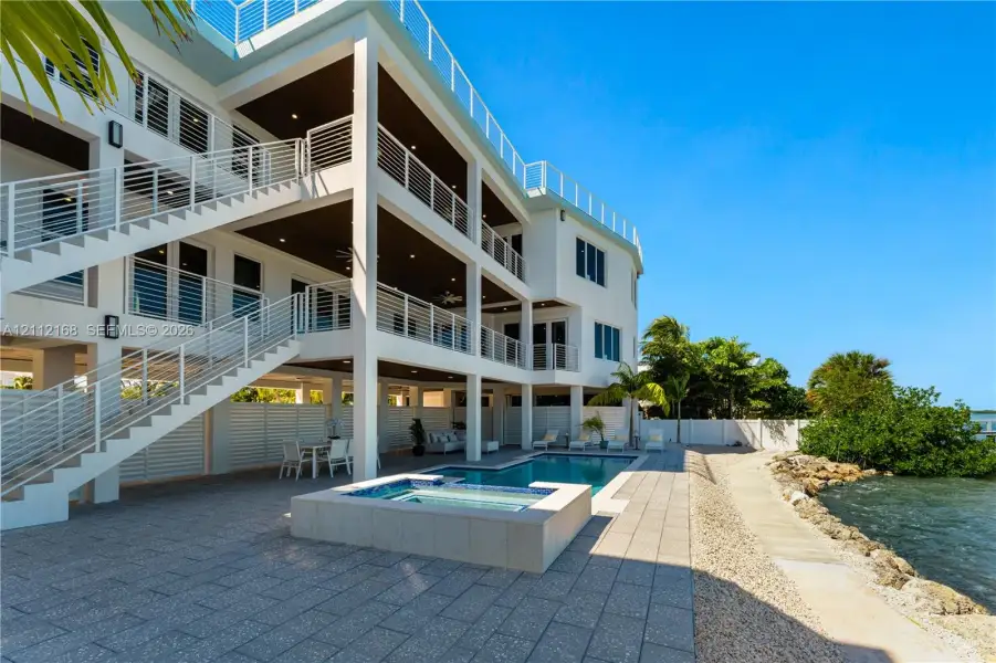 Multi-level residence featuring tiered outdoor balconies with horizontal railings, stone-tiled patio, in-ground swimming pool, and integrated spa Multi-level residence featuring tiered outdoor balconies with horizontal railings, stone-tiled patio, in-ground swimming pool, and integrated spa