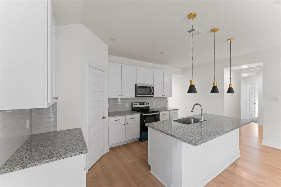 Kitchen with white cabinetry, stainless steel appliances, sink, and an island with sink