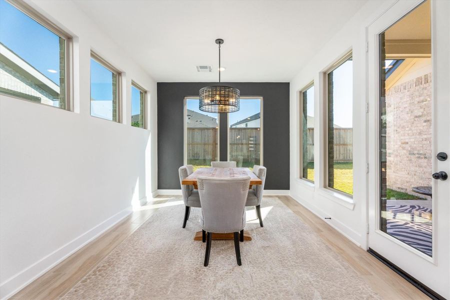 Bright dining area with large windows, modern lighting, and a cozy rug. Features a stylish table, chairs, and a view of the backyard through glass doors. Perfect for natural light and entertaining.