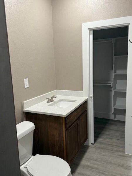 Half bathroom with vanity, toilet, wood finished floors, and a textured wall