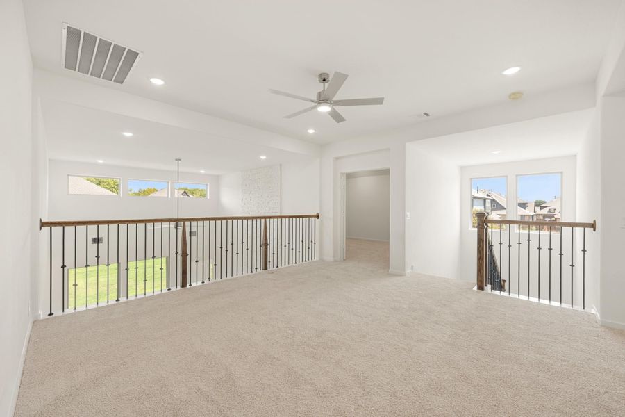 Open upstairs loft with carpet flooring, ceiling fan, and iron stair railings on both sides