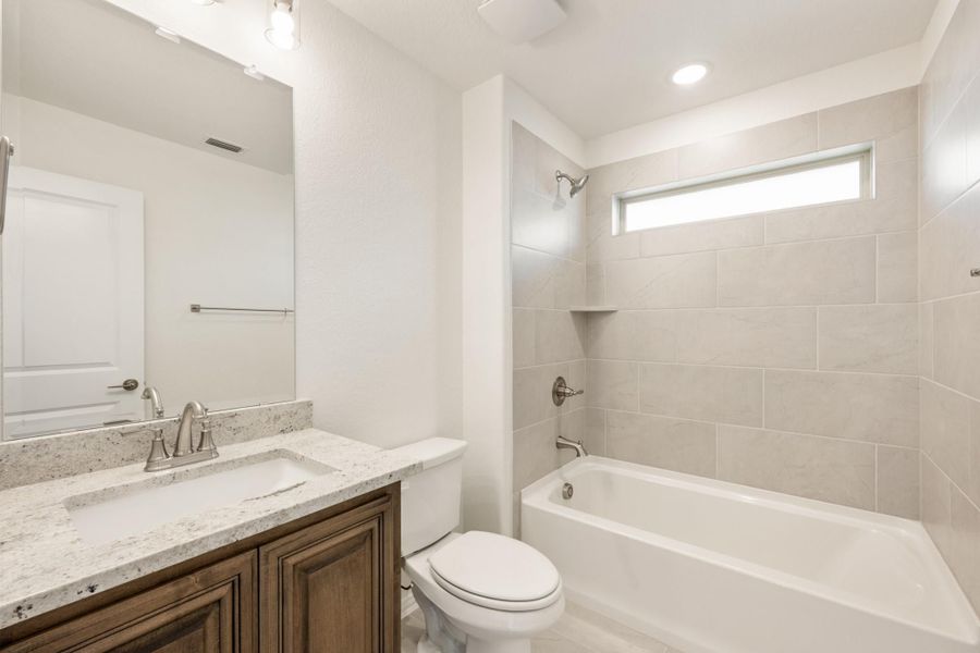 Bathroom with granite vanity, wood cabinets, and tiled tub-shower combo with small window Bathroom with granite vanity, wood cabinets, and tiled tub-shower combo with small window