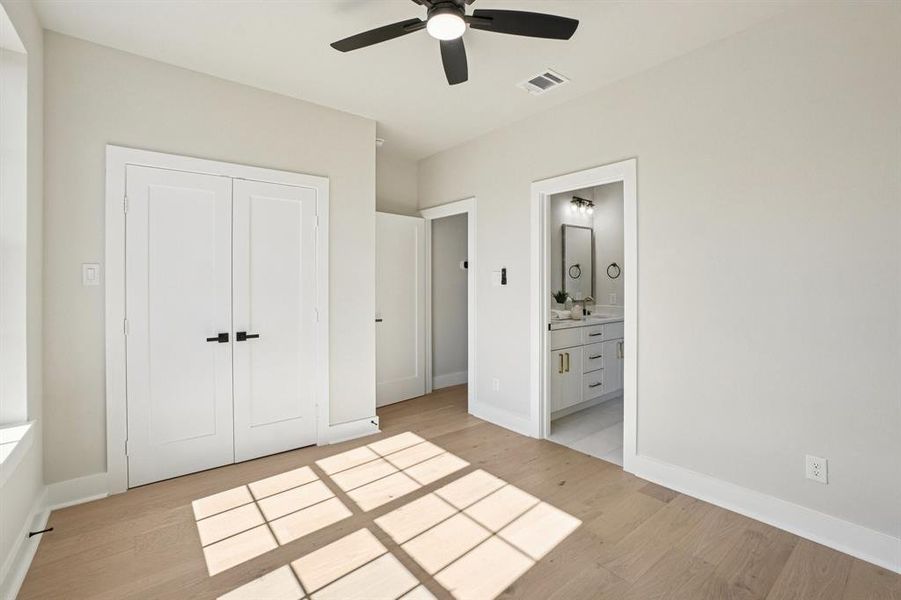 Unfurnished bedroom with light wood-style flooring, connected bathroom, a ceiling fan, and a closet