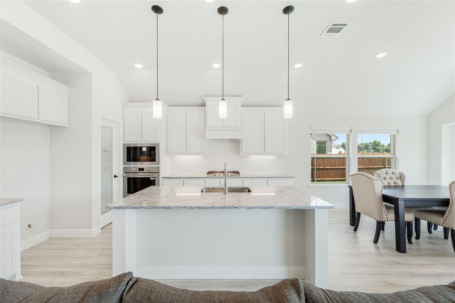 Open kitchen with white cabinets, granite island, pendant lights, and stainless steel appliances, open to dining area