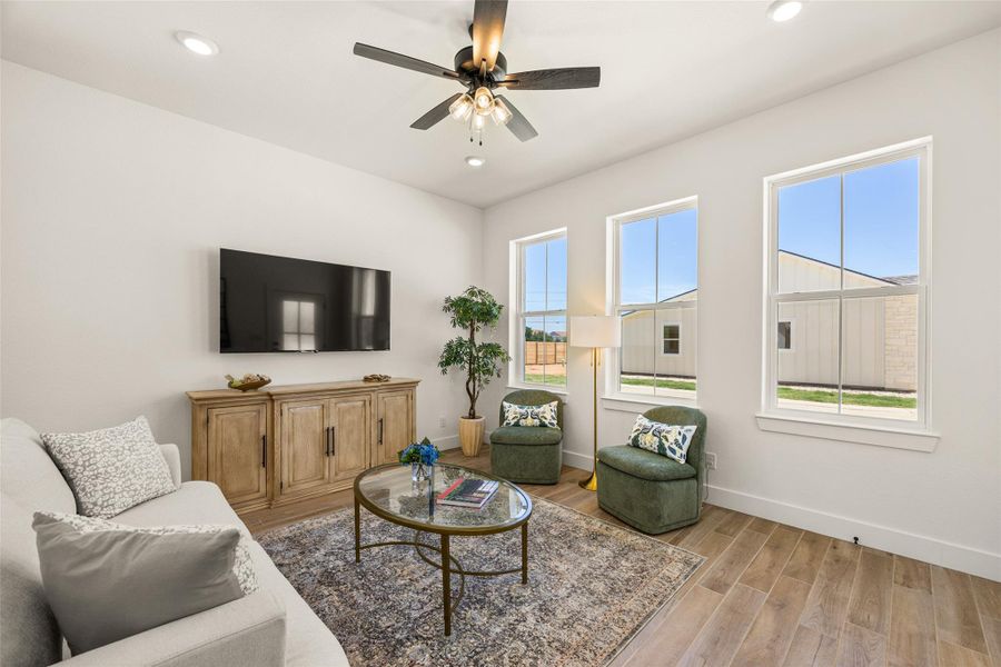Well-lit living area featuring rich hardwood flooring and a stylish ceiling fan.