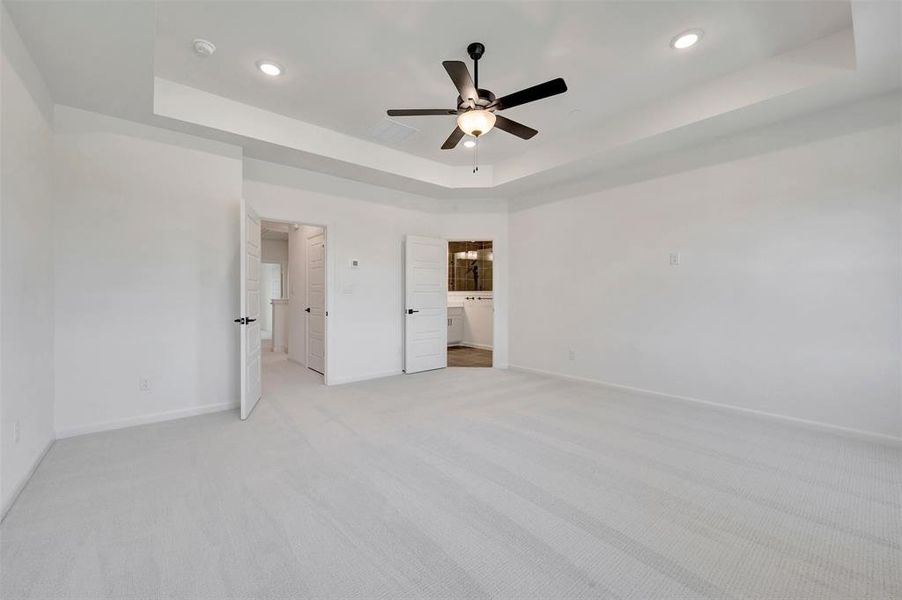 Spacious room featuring light-toned carpet flooring, a tray ceiling with recessed lighting, and a ceiling fan with light fixture Spacious room featuring light-toned carpet flooring, a tray ceiling with recessed lighting, and a ceiling fan with light fixture