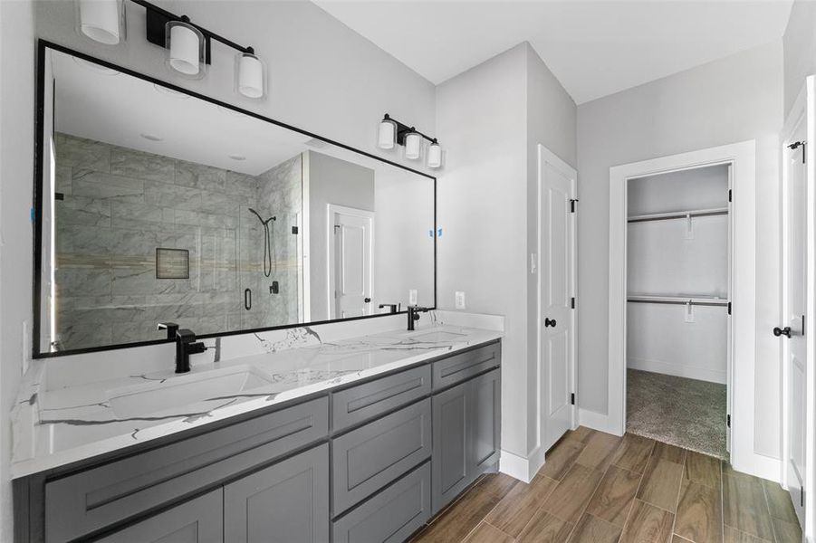 Full bathroom featuring a shower stall, a spacious closet, double vanity, and wood finish floors