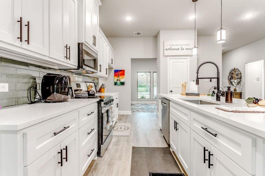 Kitchen featuring sink, decorative light fixtures, light hardwood / wood-style floors, white cabinetry, and stainless steel appliances