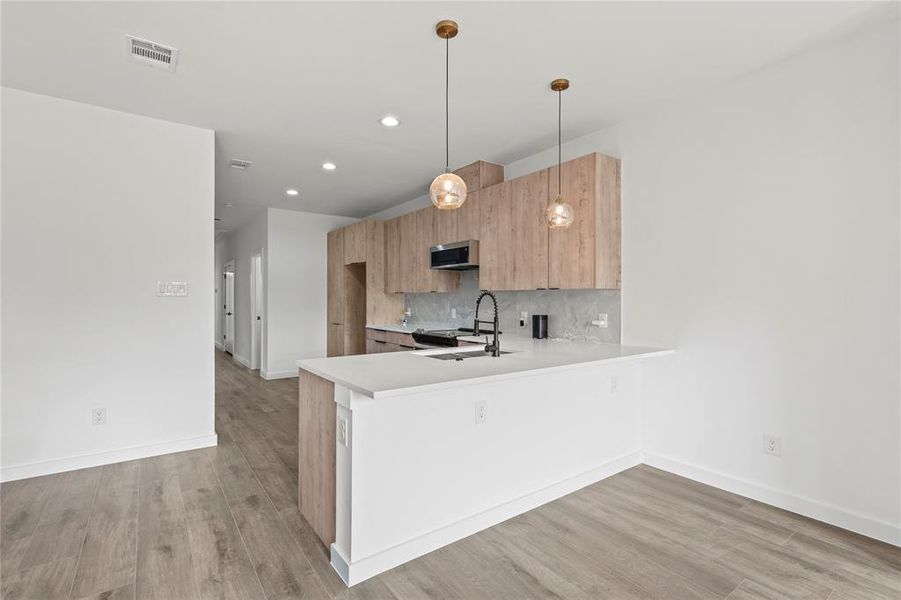 Kitchen with sink, hanging light fixtures, light wood-type flooring, tasteful backsplash, and kitchen peninsula