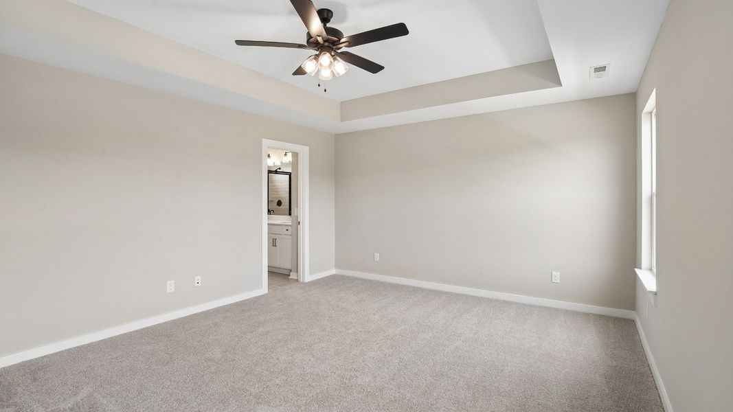 Bedroom with tray ceiling, windows, and en-suite primary bathroom