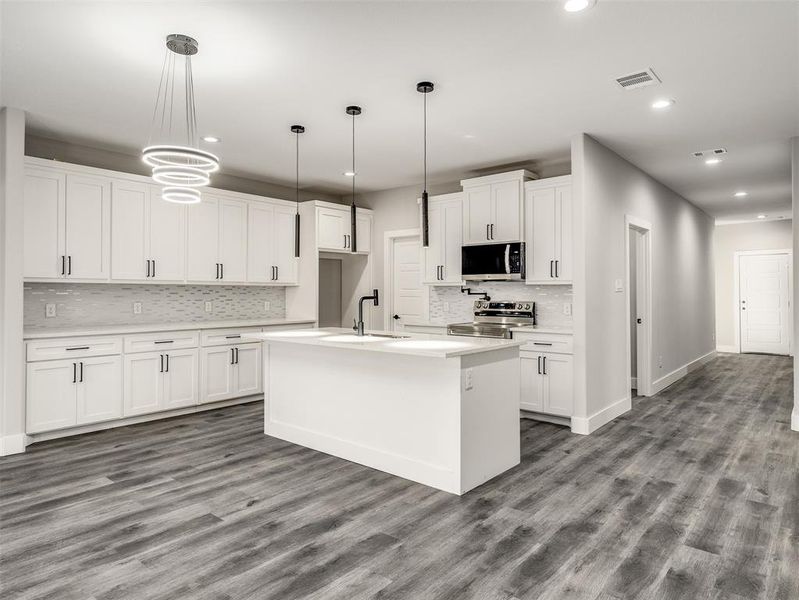 Kitchen featuring pendant lighting, white cabinetry, stainless steel appliances, and an island with sink