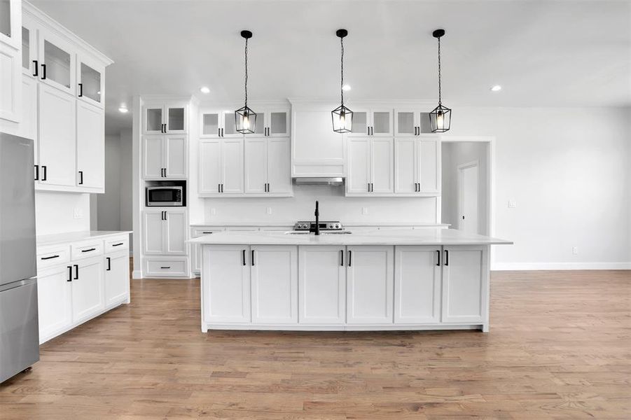 Kitchen with appliances with stainless steel finishes, light wood-type flooring, pendant lighting, and an island with sink