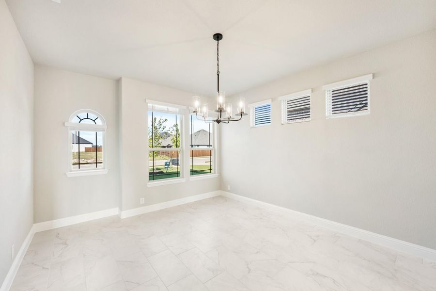 Empty dining room with chandelier, marble tile floors, and multiple windows with backyard view