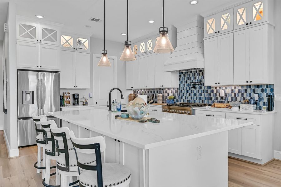 The oversized quartz island creates the perfect gathering space for entertaining after a day at the beach. Designer lighting and clean finishes give the kitchen a polished coastal feel.