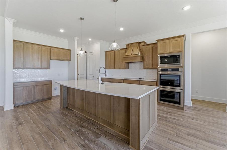 Spacious kitchen featuring a large central island with a solid surface countertop, light wood-finish cabinetry, a built-in double oven, and a patterned tile backsplash